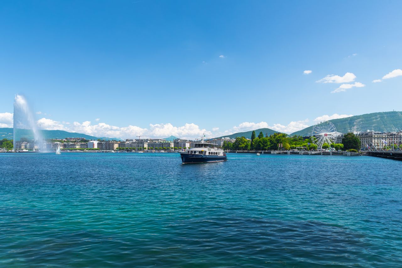 Beautiful view of Lake Geneva featuring the Jet d'Eau and a Ferris wheel under a sunny blue sky.